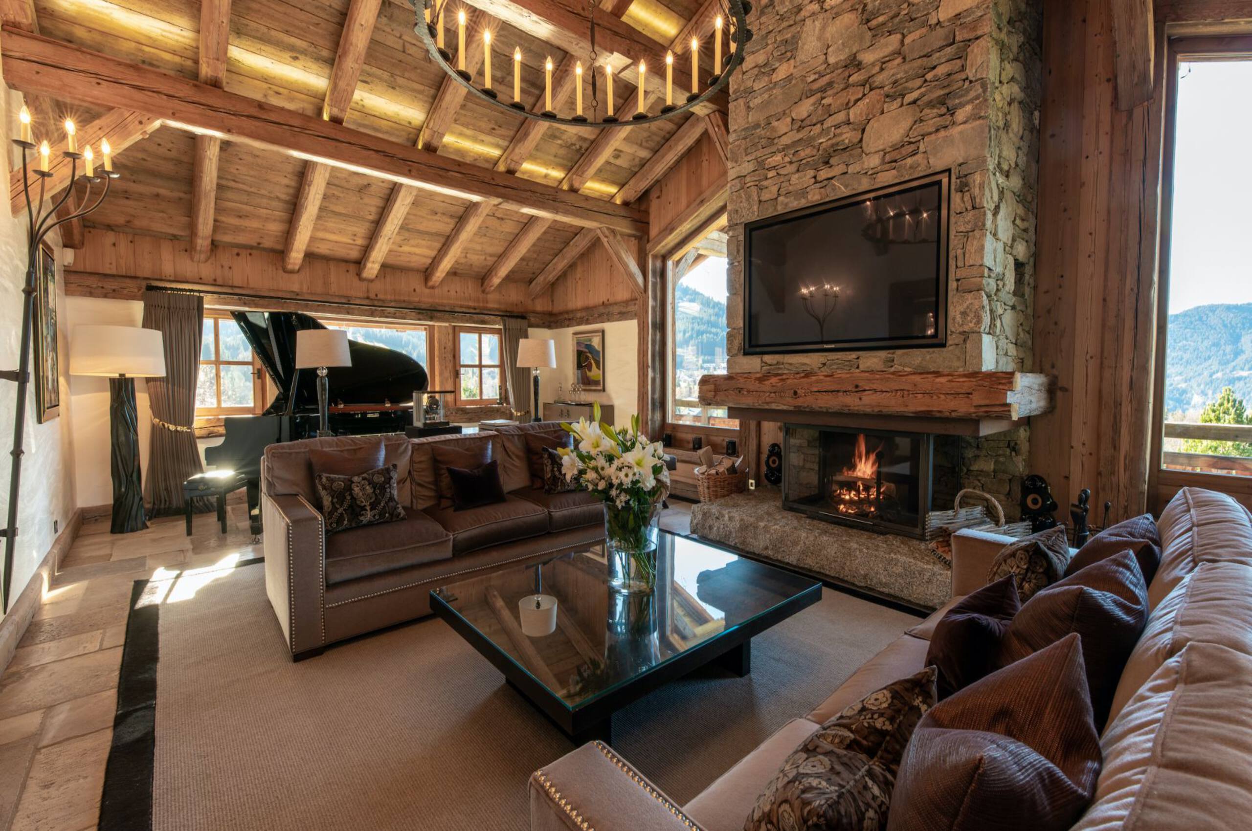 chalet-aliah-livingroom-fireplace-piano-tv-mountainviews-heighceiling-elegant-alpine-interiors-luxury-rental-megeve